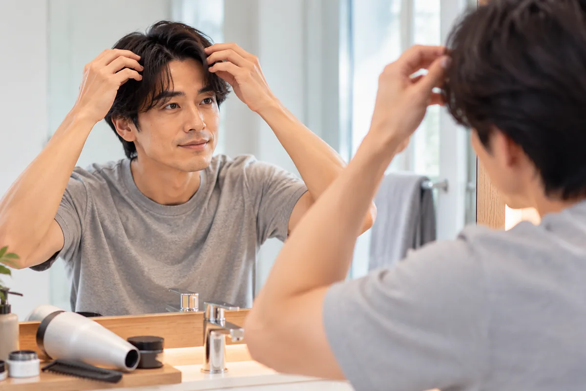 朝の洗面所の鏡の前で前髪にスタイリング剤をなじませる男性